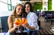 © F8  \ Suport Ukraine - Young women drinking aperol spritz, clink glasses with friends, looking at camera in modern cafe