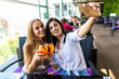 © F8  \ Suport Ukraine - Two attractive young woman take a selfie while sitting and chilling in the summer terrace of city cafe