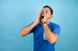 Young handsome man wearing blue casual t-shirt over isolated blue background shouting and screaming loud to side with hands on mouth. Communication concept.