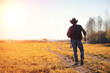 © alexkich - A man cowboy hat and a loso in the field. American farmer in a field wearing a jeans hat and with a loso. A man is walking across the field in a hat