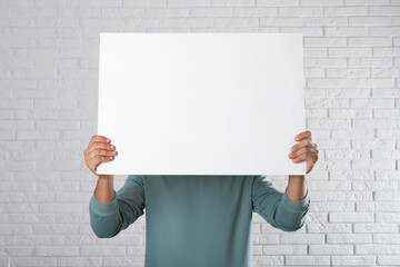 Wall Mural - man holding blank poster near white brick wall. mockup for design