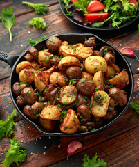 Wall Mural - Baked potato with mushrooms and herbs in iron cast pan on wooden table