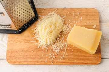 Wall Mural - Wedge of traditional italian hard cheese Grana Padano or Parmesan, grated cheese and stainless steel kitchen grater on a wood cutting board over white wood table.