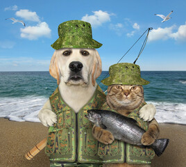 Wall Mural - A dog fisher with a fishing rod hugs a cat with big fish on a beach of the sea.