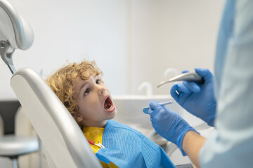 Wall Mural - Cute young boy visiting dentist, having his teeth checked by female dentist in dental office.