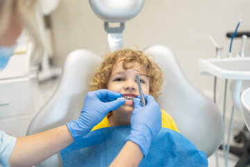 Wall Mural - Cute young boy visiting dentist, having his teeth checked by female dentist in dental office.