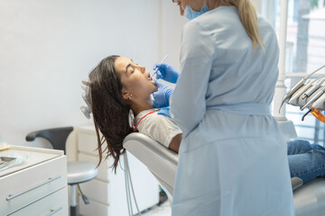 Wall Mural - Female dentist in dental clinic providing examination and treatment of oral cavity for female patient.