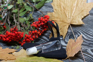 Wall Mural - Medical mask and antiseptic. Nearby is a rowan branch and maple leaves. On black pine boards.