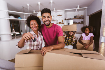 Smiling family carrying boxes into new home on moving day, holding keys in new apartment.