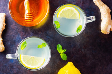 Wall Mural - Ginger tea with lemon on a dark background. Two cups of ginger tea and ingredients for its preparation