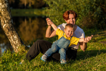 Mom and little boy sit on the river bank in the rays of the setting sun