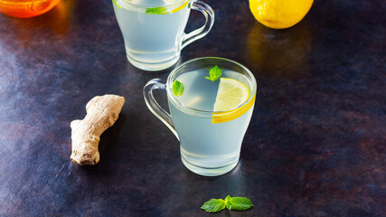 Wall Mural - Ginger tea with lemon on a dark background. Two cups of ginger tea and ingredients for its preparation