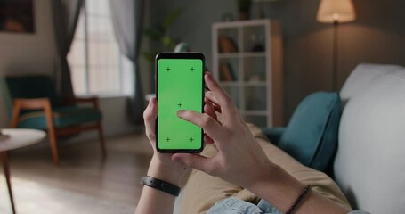 Close up shot of man lying on couch and using smart phone with chroma key green screen, doing various taps, swipes and scrolls - technology, communication 4k video template