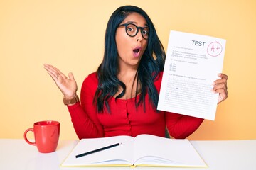 Canvas Print - Beautiful latin young woman with long hair showing a passed exam scared and amazed with open mouth for surprise, disbelief face