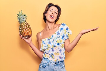 Young beautiful woman holding pineapple celebrating achievement with happy smile and winner expression with raised hand