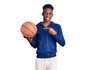 © Krakenimages.com - Young african american man holding basketball ball smiling happy pointing with hand and finger
