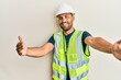 © Krakenimages.com - Handsome man with beard wearing safety helmet and reflective jacket looking at the camera smiling with open arms for hug. cheerful expression embracing happiness.