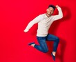 © Krakenimages.com - Young handsome latin man wearing casual clothes smiling happy. Jumping with smile on face doing ok sign with thumbs up over isolated red background