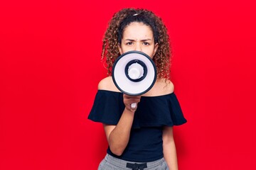 Wall Mural - Adorable latin teenager girl with angry expression. Screaming loud using megaphone standing over isolated red background