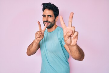 Handsome hispanic man with beard wearing casual clothes smiling looking to the camera showing fingers doing victory sign. number two.