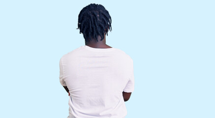 Young african american man with braids wearing casual white tshirt standing backwards looking away with crossed arms