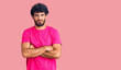 © Krakenimages.com - Handsome young man with curly hair and bear wearing casual pink tshirt skeptic and nervous, disapproving expression on face with crossed arms. negative person.