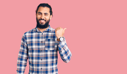 Young arab man wearing casual clothes smiling with happy face looking and pointing to the side with thumb up.