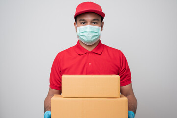 Wall Mural - Young asian delivery man in red uniform wearing protection mask and medical rubber gloves giving parcel cardboard to customer  on isolated white background. Safety deliver concept.