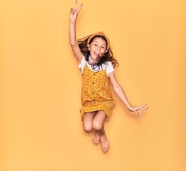 Adorable hispanic child girl wearing casual dress and diadem smiling happy. Jumping with smile on face over isolated yellow background