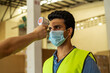 © twinsterphoto - Young Indian factory warehouse worker wearing face mask getting body temperature check with infrared thermometer scanner before working. Security measure at workplace in Coronavirus Covid 19 pandemic