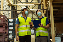 Group Of Young Factory Warehouse Workers Wearing A Protective Face Mask While Working In Logistic Industry Indoor. Asian And Indian Ethnic Men Checking Item Order During Coronavirus Covid 19 Pandemic