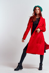 Canvas Print - emotional woman in a red coat and with a hat in full growth on a light background black boots pose model