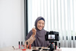© Orathai - Muslim women making video beauty vlogger bloggers doing a cosmetic makeup tutorial vlog with brushes looking camera Save clips and share them on social media live via the internet Online