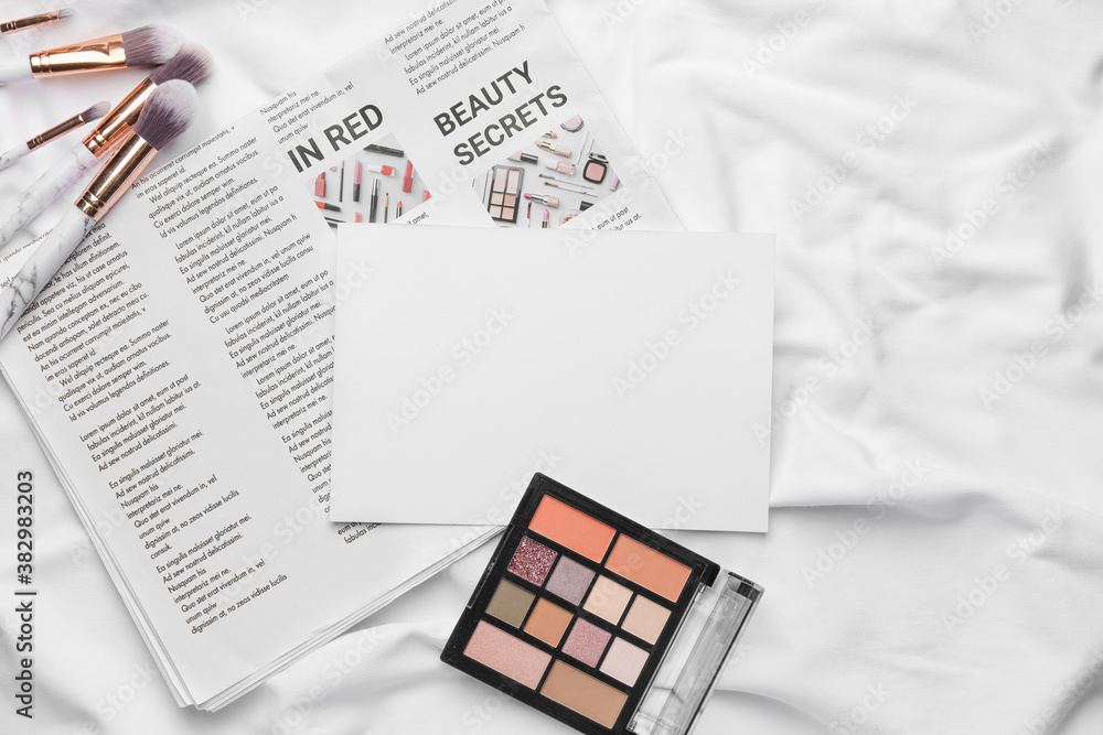 Composition with blank card, newspaper and makeup cosmetics on fabric background