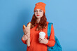 © sementsova321 - Portrait of unhappy woman wearing hat and casual sweater, holding paper bag with baguettes and coffee to go, looks at camera with sad look, being tired from hard studying, against blue wall.