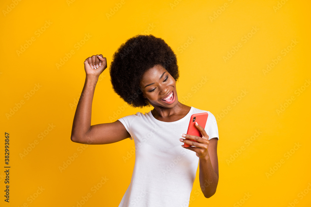 Photo portrait of young woman celebrating victory holding one fist up wearing casual white t-shirt isolated on vivid yellow colored background - obrazy, fototapety, plakaty 