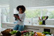 © Prins Productions - African American smiling female researching recipes on digital tablet leaning against counter in clean kitchen.