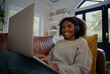Cheerful young african woman relaxing at home watching web series with headphones sitting on couch