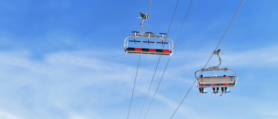 Wall Mural - chairlifts one empty and other  transporting people in a winter resort under blur sky