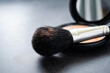 Wall Mural - Close-up of a black makeup brush with flesh-colored powder at the end. On the background of an open box with a mirror and pink powder. Dark, almost black background. Copy space