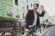 © mad_production - Low angle shot of a cheerful mature man waving at someone, crossing the road with his bicycle