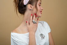 Close-up From The Side: A Brunette With Radiant Skin, Bright Makeup And Professional Hair In A White Blouse Holds Her Fingers To Her Neck, Showing Off A Silver Ring In The Shape Of A Bird.