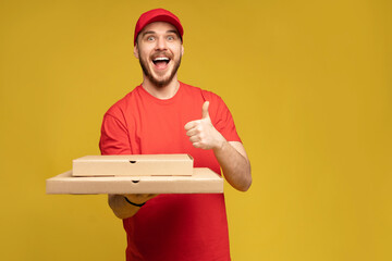 Wall Mural - Photo of happy man from delivery service in red t-shirt and cap giving food order and holding pizza box isolated over yellow background