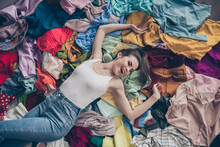 High Angle Above View Photo Of Cheerful Funny Lady Stay Home Spring Cleaning Household Lying Among Many Clothes Heap Stack Floor Shopper Surrounded Sales Stuff Do Not Care Mess Indoors