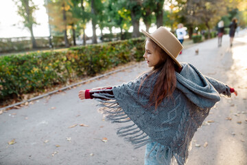 Freedom of movement. Little girl 7 years old in a warm cape and hat is dancing on the alley of the park at sunset in autumn
