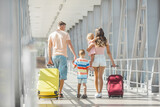 Fototapeta Tulipany - Happy family at the airport with suitcases traveling
