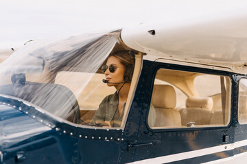 Woman pilot in airplane cabin, wearing headset and sunglasses.