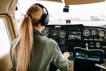 Back view over woman pilot flying an airplane, wearing headset.