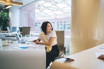 Successful Japanese freelancer smiling at desk with modern laptop technology for distance job, cheerful Chinese executive employee with digital cellphone gadget in hand rejoicing during working day