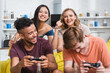 © LIGHTFIELD STUDIOS - KYIV, UKRAINE - JULY 28, 2020: selective focus of excited asian woman showing winner gesture near multicultural friends playing video game